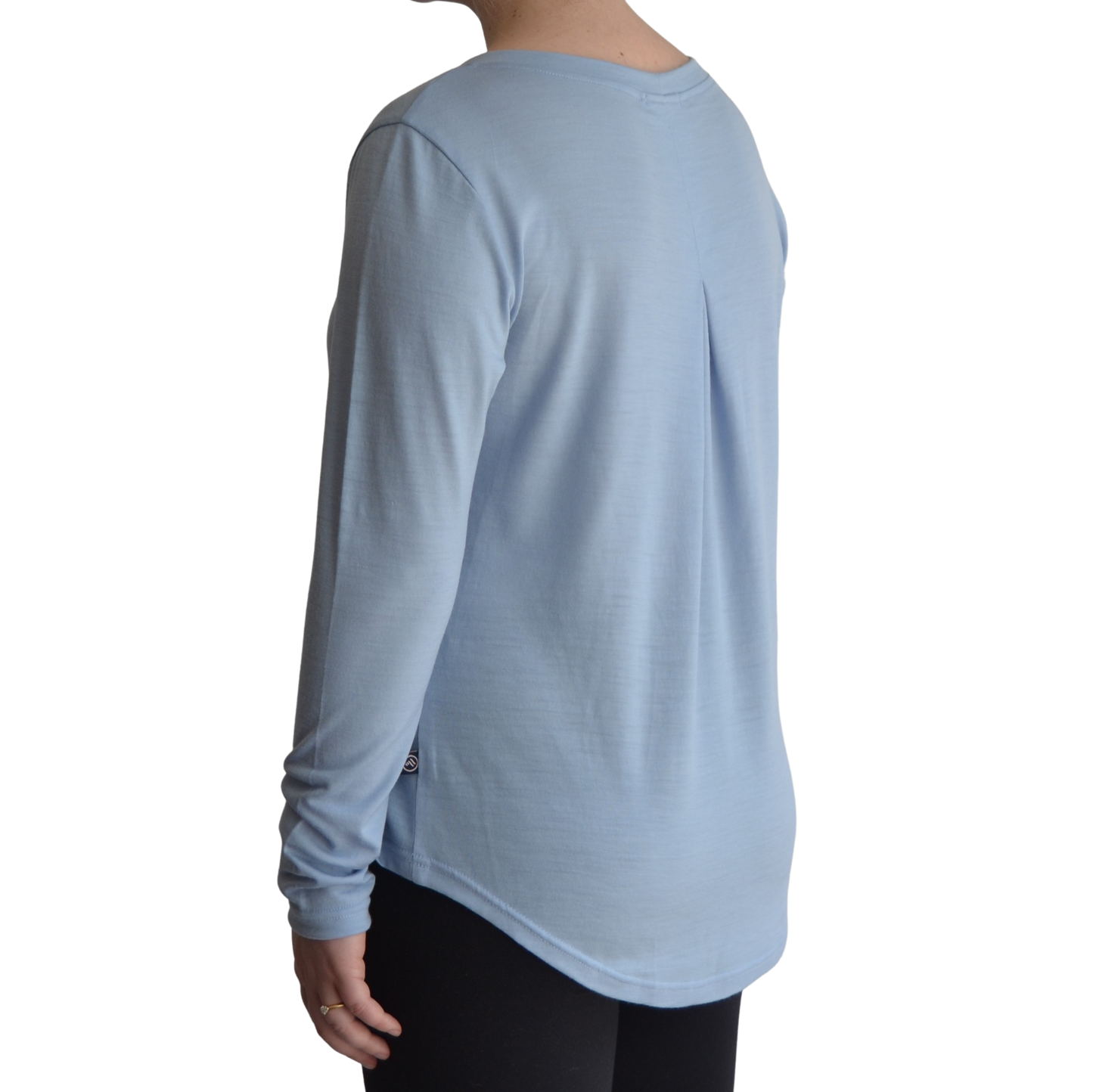 Links long sleeve merino top in ice blue colour. The model is standing on a 45 degree angle facing the back showing a dropped back hemline and box pleat.