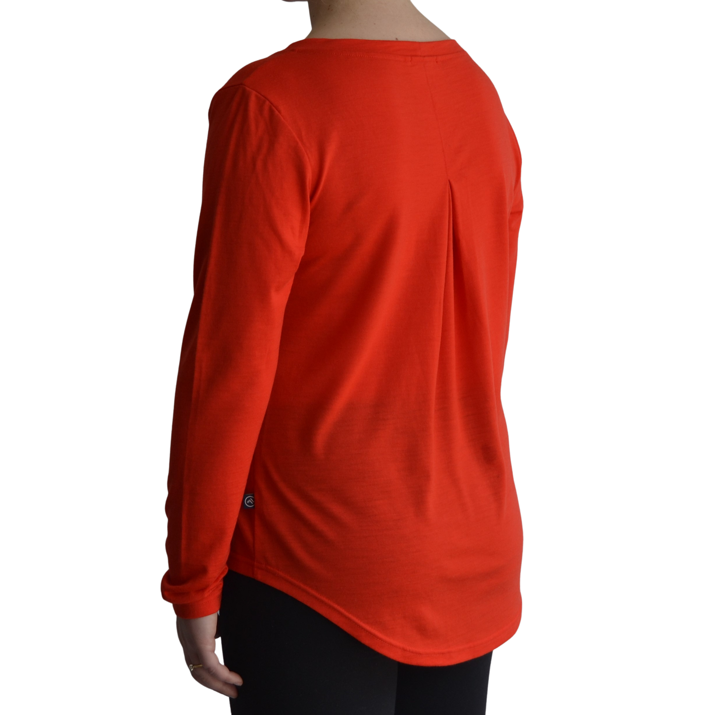 Links long sleeve merino top in mandarin colour. The model is standing on a 45 degree angle facing the back showing a dropped back hemline and box pleat.