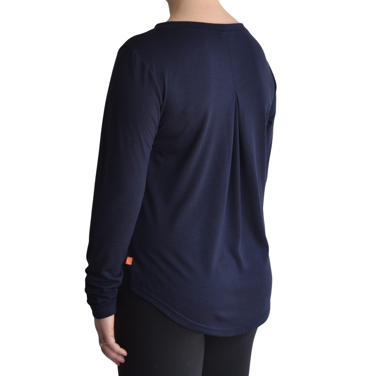 Links long sleeve merino top in navy blue colour. The model is standing on a 45 degree angle facing the back showing a dropped back hemline and box pleat.
