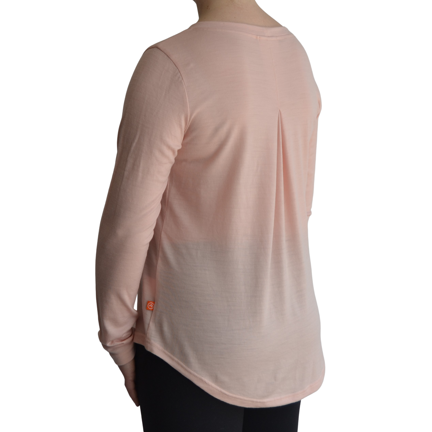 Links long sleeve merino top in petal light pink colour. The model is standing on a 45 degree angle facing the back showing a dropped back hemline and box pleat.