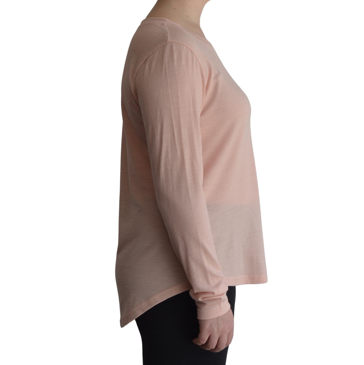 Links long sleeve merino top in petal light pink colour, model is standing in profile showing the side view of the shirt with a scooped hemline that drops lower at the back.