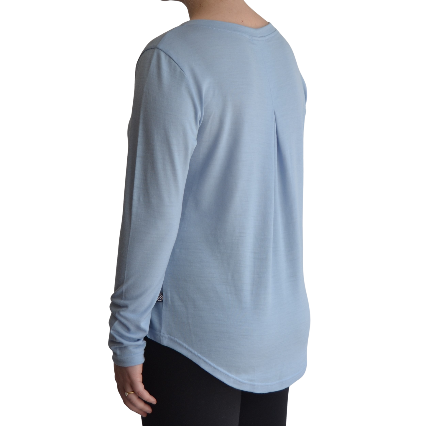 Links long sleeve merino top in ice blue colour. The model is standing on a 45 degree angle facing the back showing a dropped back hemline and box pleat. 