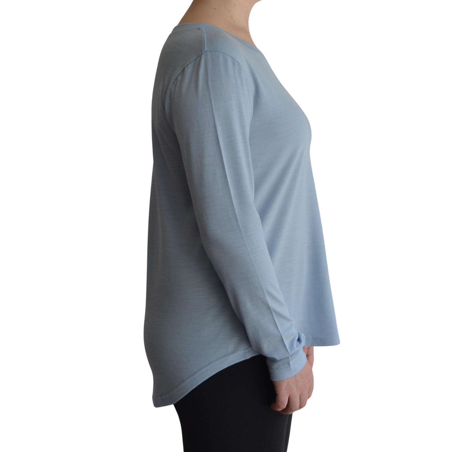 Links long sleeve merino top in ice blue colour, model is standing in profile showing the side view of the shirt with a scooped hemline that drops lower at the back. 