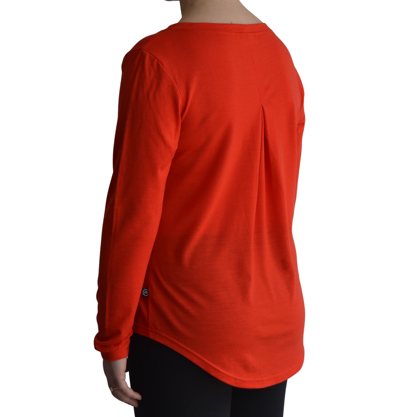 Links long sleeve merino top in mandarin colour. The model is standing on a 45 degree angle facing the back showing a dropped back hemline and box pleat. 