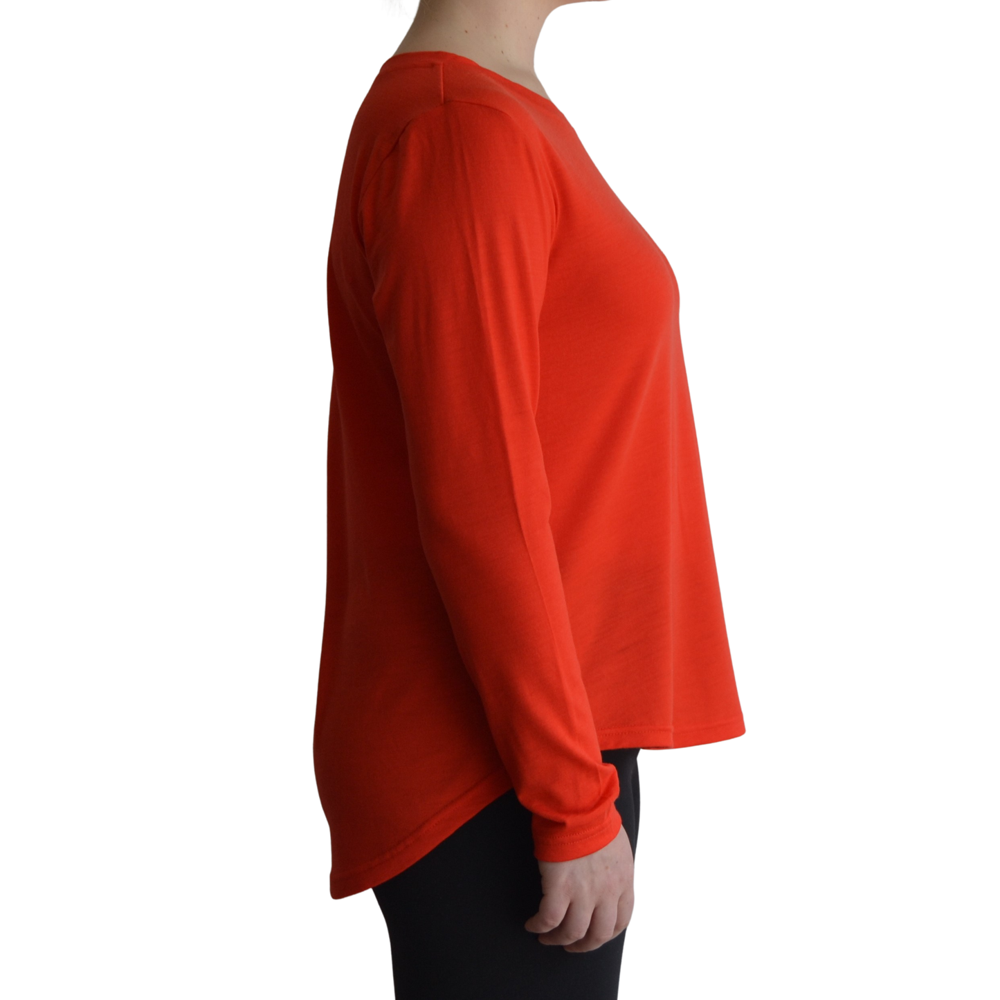 Links long sleeve merino top in mandarin colour, model is standing in profile showing the side view of the shirt with a scooped hemline that drops lower at the back. 
