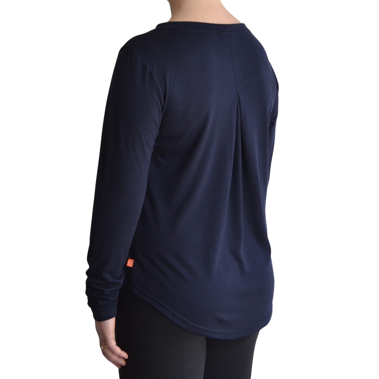 Links long sleeve merino top in navy blue colour. The model is standing on a 45 degree angle facing the back showing a dropped back hemline and box pleat. 