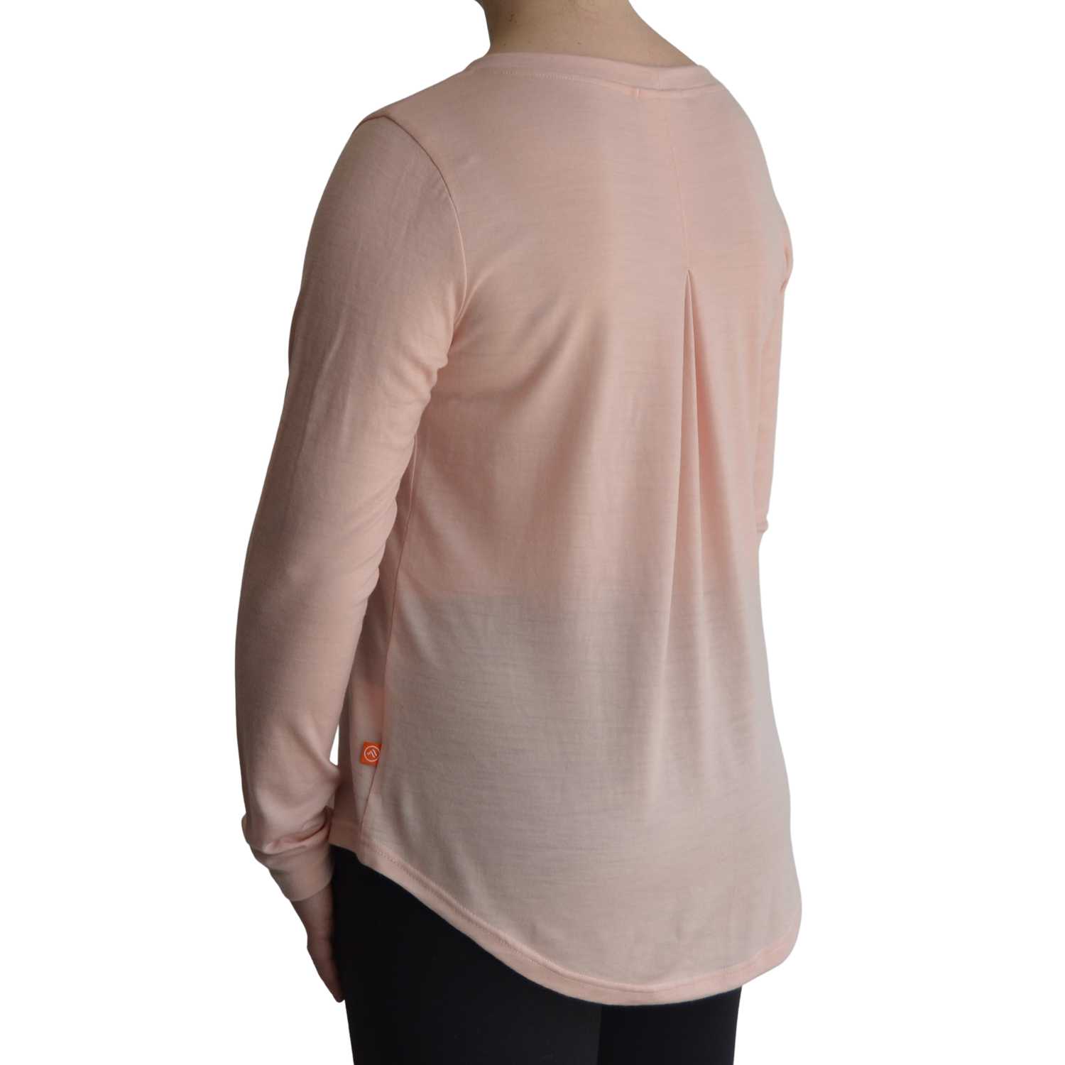 Links long sleeve merino top in petal light pink colour. The model is standing on a 45 degree angle facing the back showing a dropped back hemline and box pleat. 