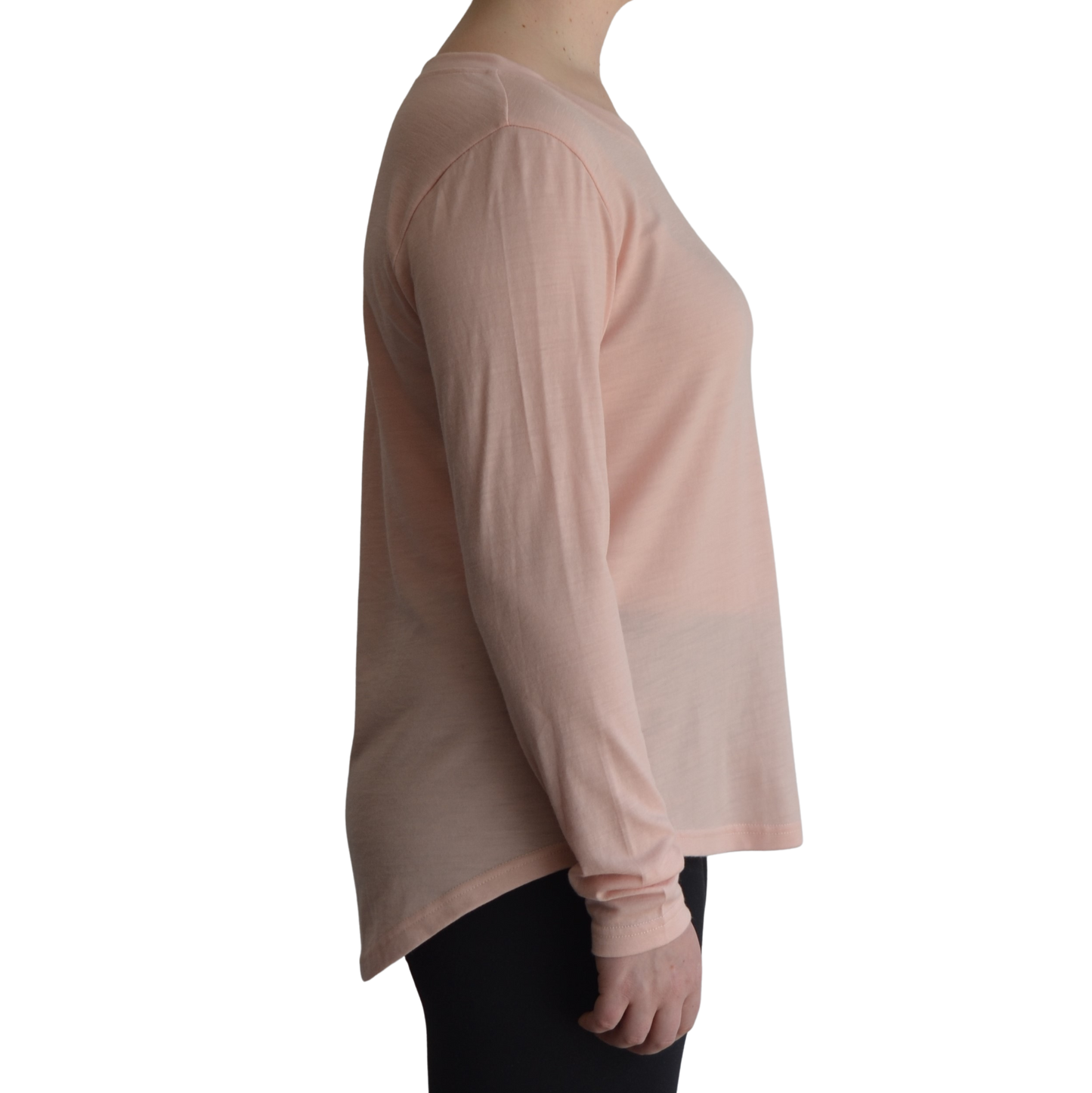 Links long sleeve merino top in petal light pink colour, model is standing in profile showing the side view of the shirt with a scooped hemline that drops lower at the back. 