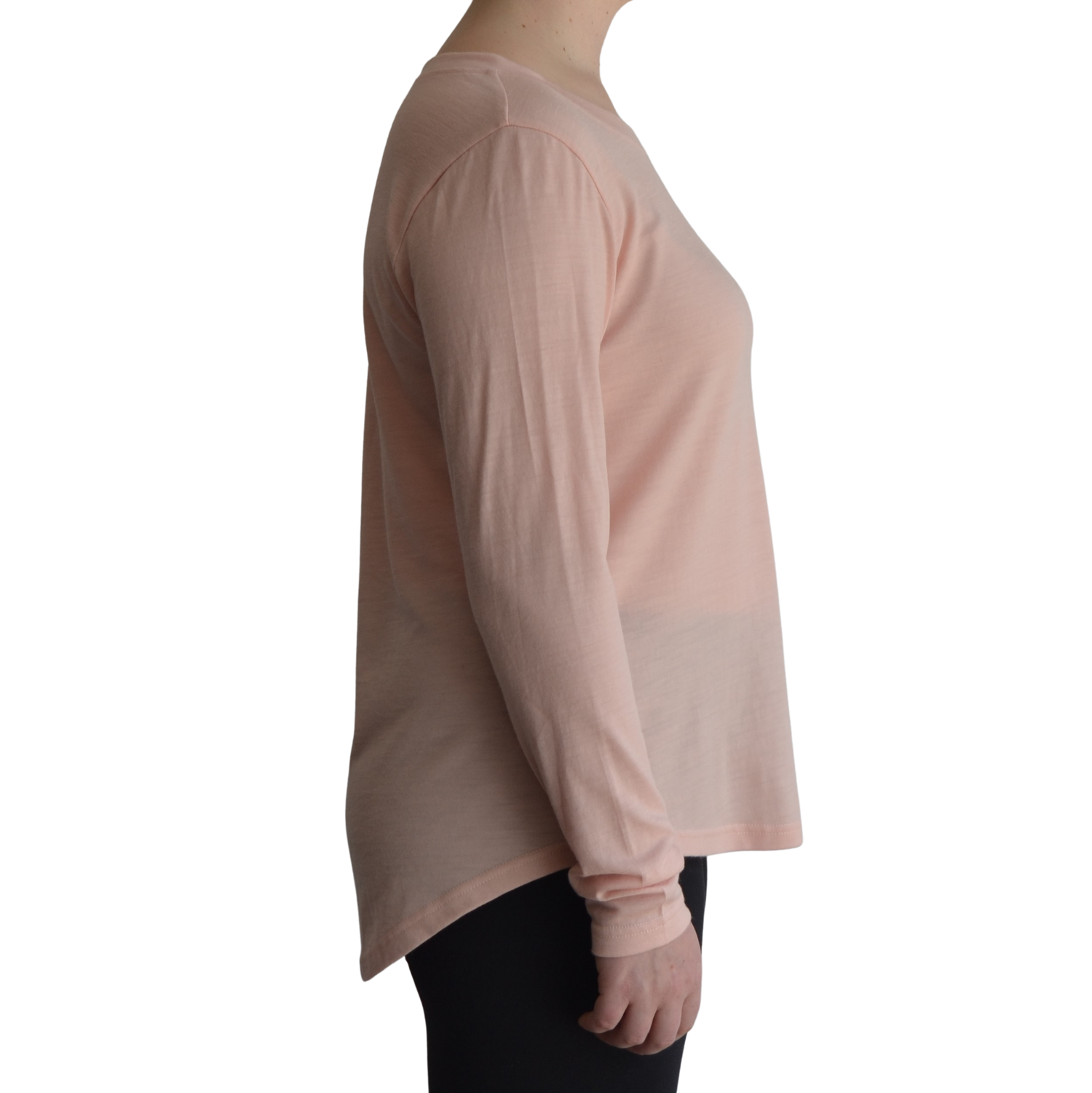 Links long sleeve merino top in petal light pink colour, model is standing in profile showing the side view of the shirt with a scooped hemline that drops lower at the back. 